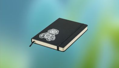 A black hardcover notebook with an elastic band and a sticker of a smiling robot on the cover, against a blurred blue and green background.